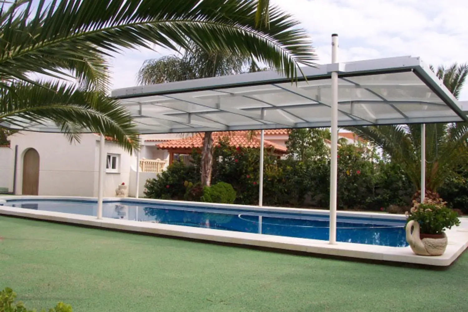 Langes Schwimmbecken mit zur Seite geschobener Poolüberdachung, Palmen und blauer Himmel