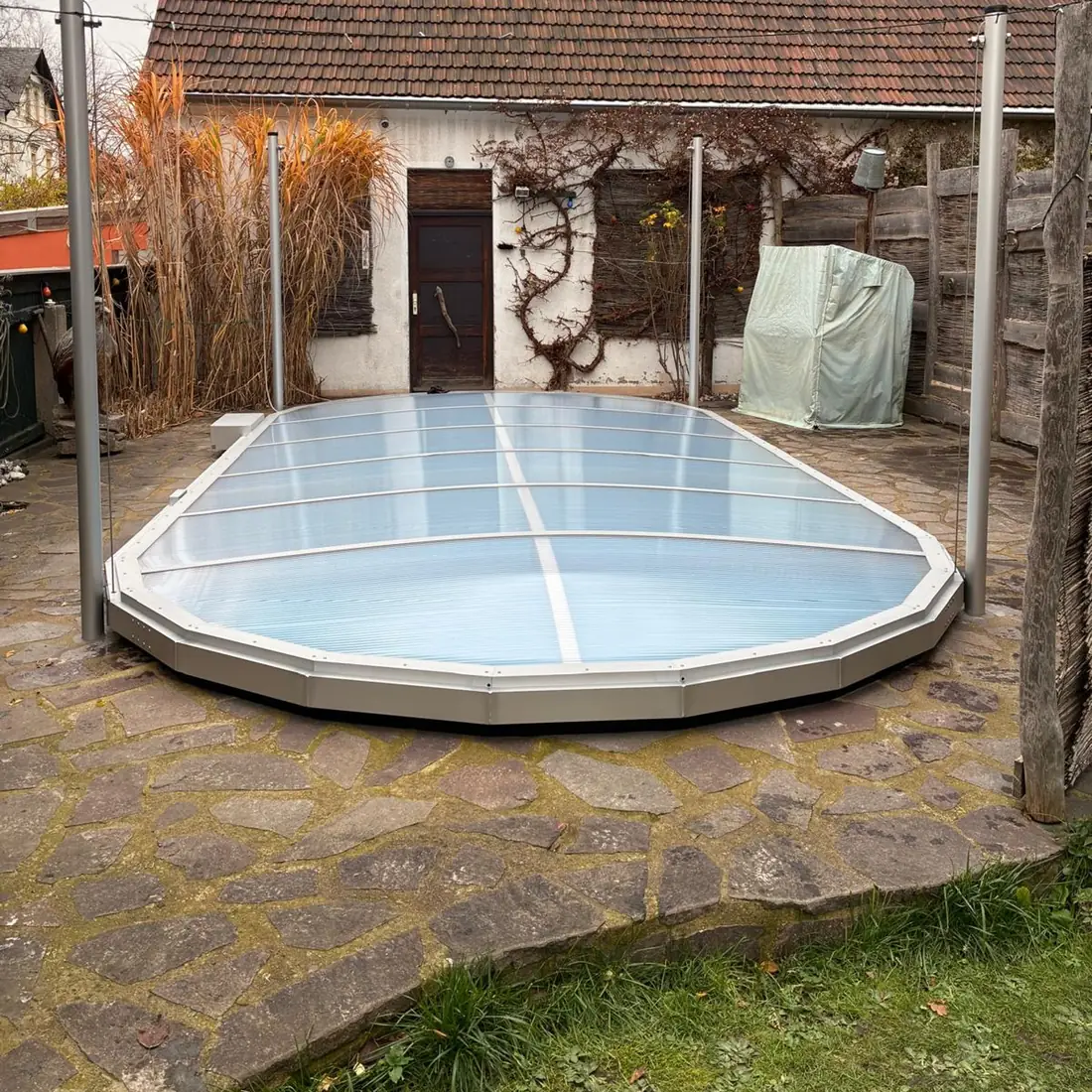 Ovalbecken mit abgesenkter Poolüberdachung, das Dach liegt geschlossen auf dem Beckenrand
