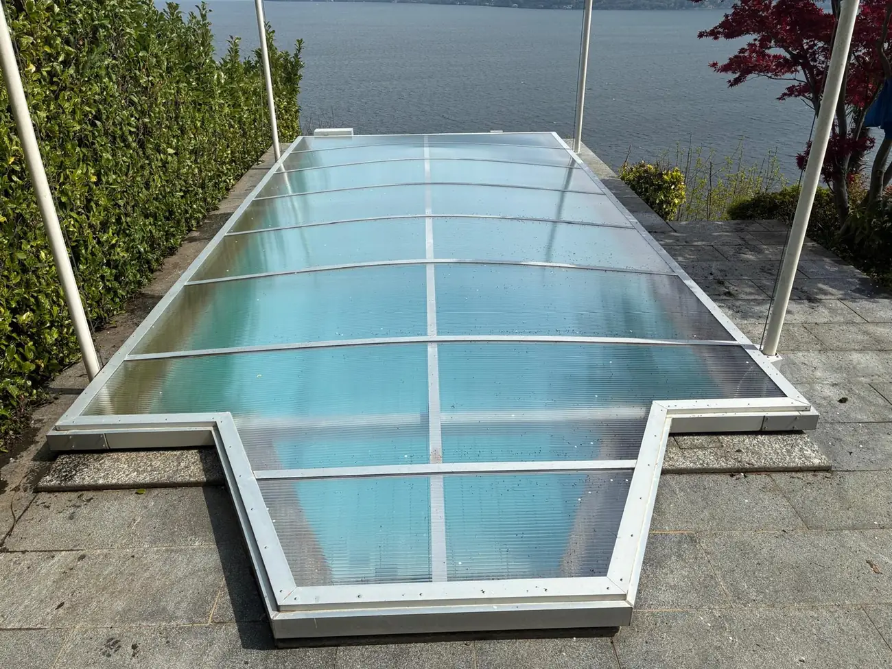 Poolüberdachung zur Hälfte geöffnet, die Dachelemente sind übereinander geschoben, im Hintergrund ein See
